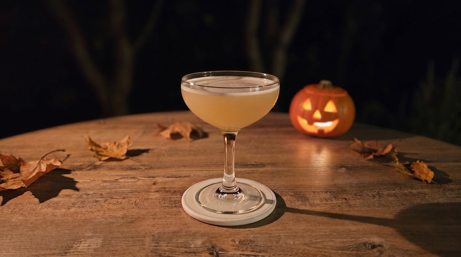 Cocktail Corpse Reviver dans une coupe, à la lueur d'une citrouille d'Halloween et de feuilles mortes