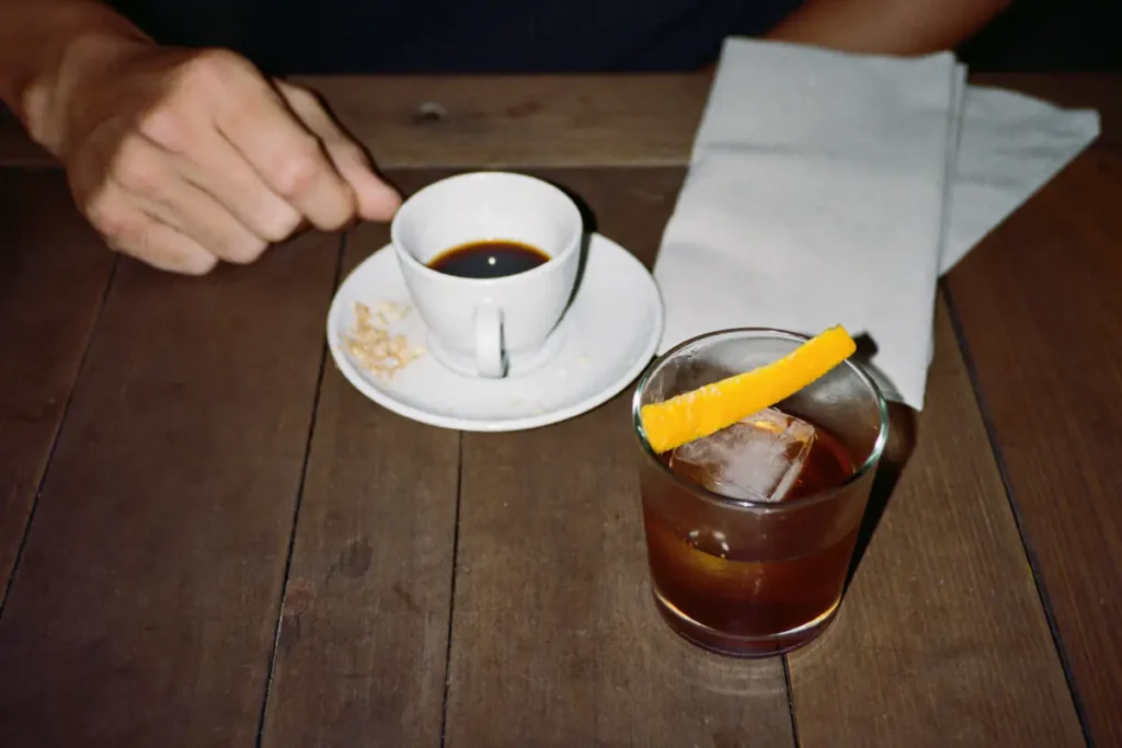 Amaro sur un glaçon avec un zeste d'orange, servi à côté d'un expresso en fin de repas