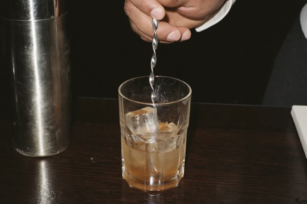 Cocktail remué à la cuillère de bar à côté d'un shaker en inox