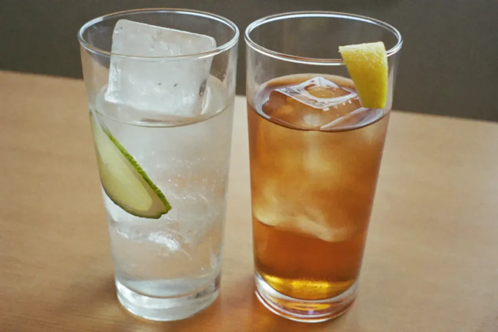 Deux highballs remplis de glace : un gin tonic au citron vert et un whisky soda au zeste de citron