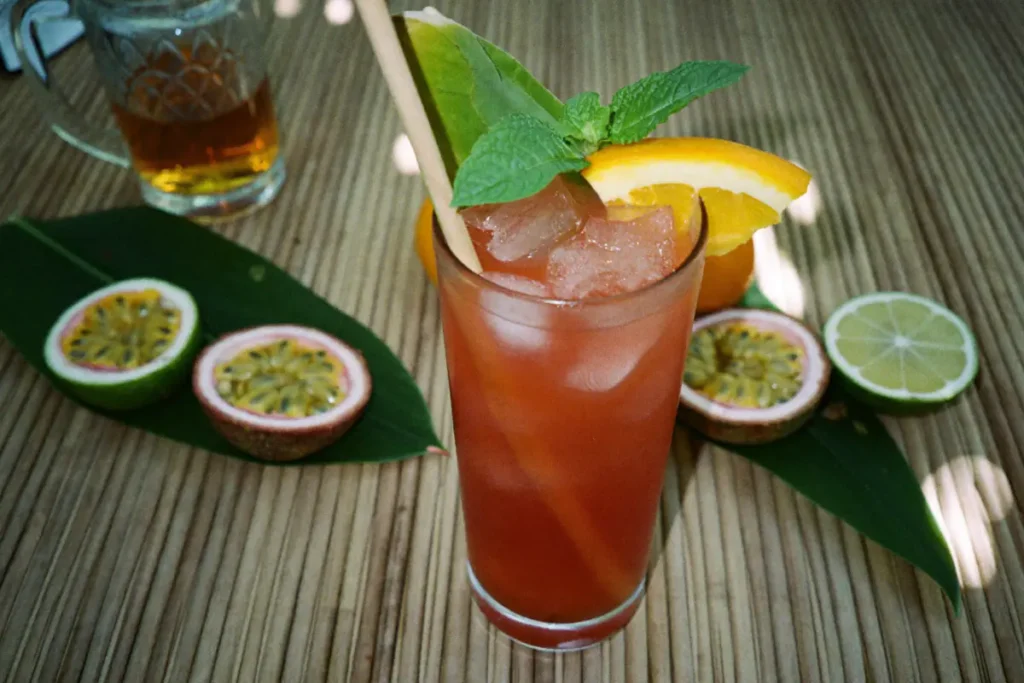 Cocktail tiki Zombie sur glace pilée, décoré de menthe et d'orange, entouré de fruits de la passion et de citrons verts
