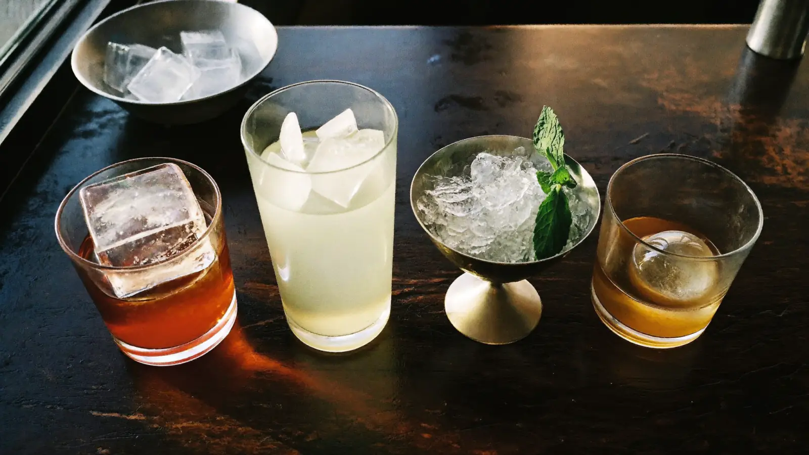 Quatre cocktails servis avec des glaces différentes : gros cube, glaçons standard, glace pilée à la menthe et sphère de glace