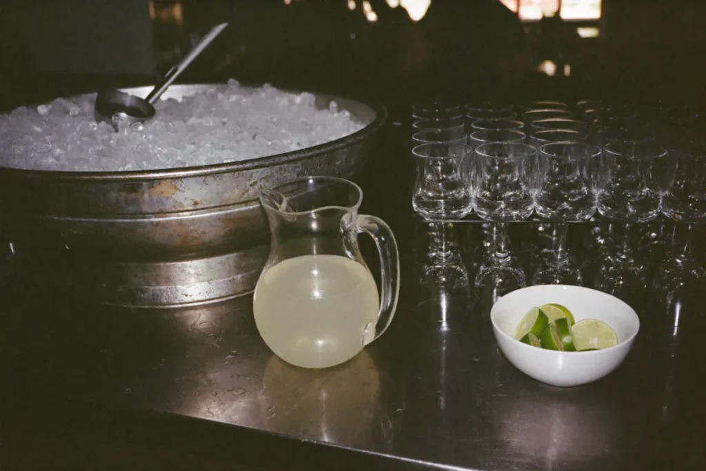 Bac en métal rempli de glaçons avec une pelle, carafe de citronnade et verres prêts pour une soirée