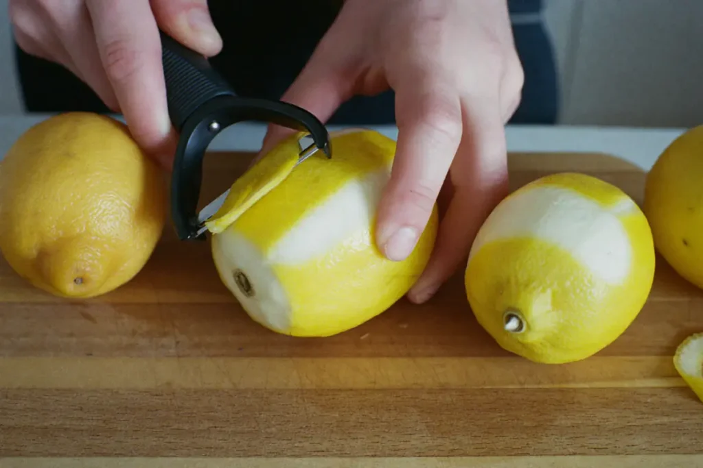 Zestes de citron prélevés à l'économe, sans la partie blanche, sur une planche en bois