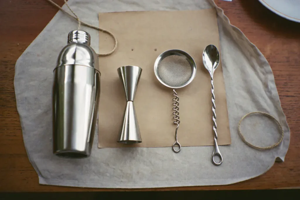 Kit cocktail en inox posé sur un linge : shaker trois pièces, doseur, passoire et cuillère de bar torsadée