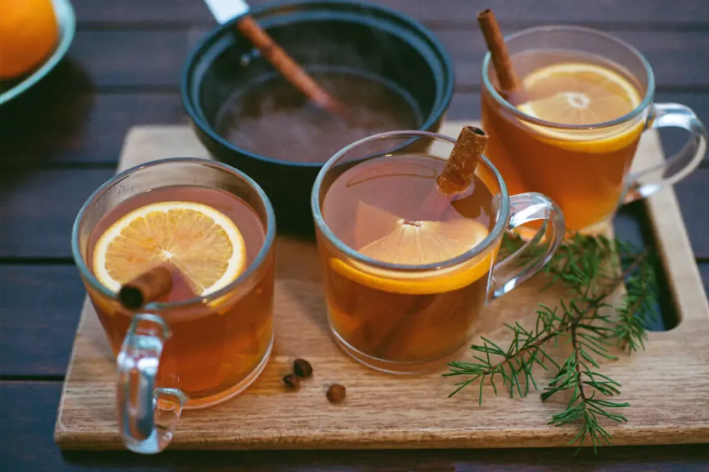 Trois mugs de punch chaud de Noël au rhum avec une rondelle d'orange et un bâton de cannelle, casserole à l'arrière