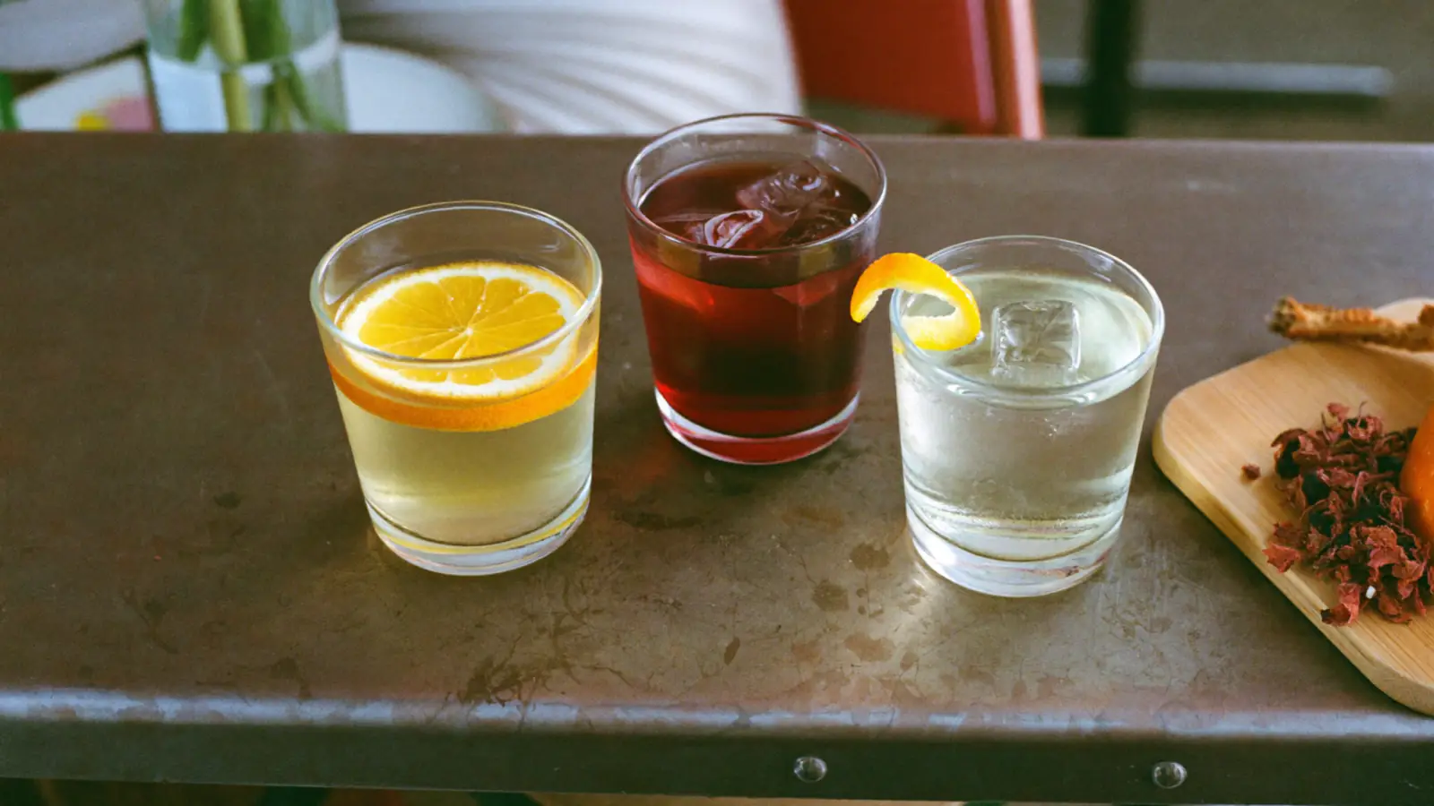 Trois apéritifs français sur glace sur un comptoir de bistrot : un vin blanc aromatisé à l'orange, un quinquina rouge et un apéritif à la gentiane