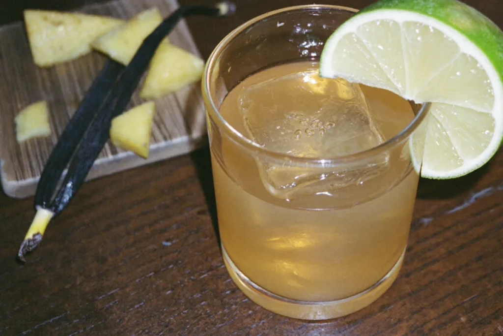 Verre de rhum arrangé ananas sur glace avec un quartier de citron vert