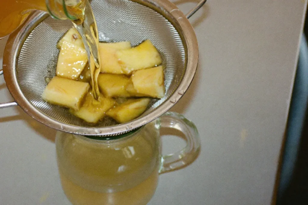 Rhum arrangé à l'ananas filtré à travers une passoire fine au-dessus d'une carafe