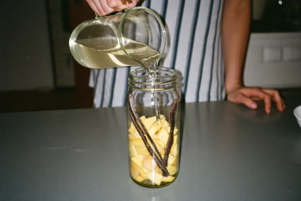 Rhum blanc versé sur des morceaux d'ananas et des gousses de vanille dans un bocal