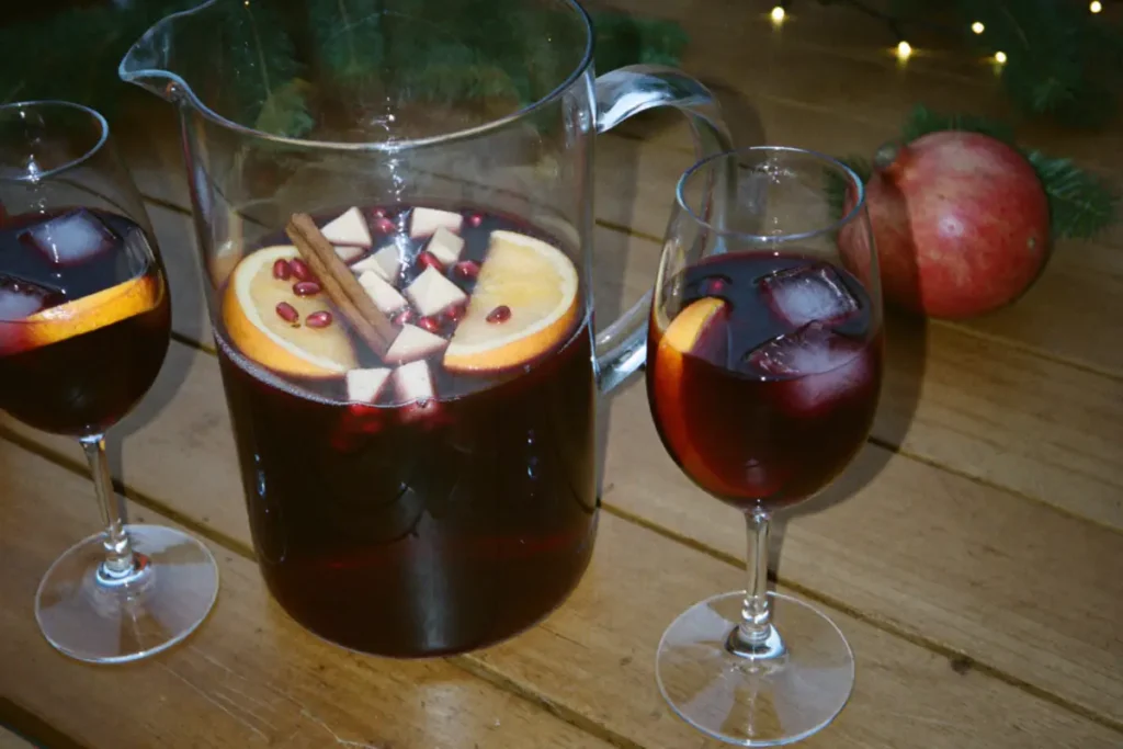 Carafe de sangria de Noël au vin rouge avec rondelles d'orange, dés de pomme, graines de grenade et bâton de cannelle