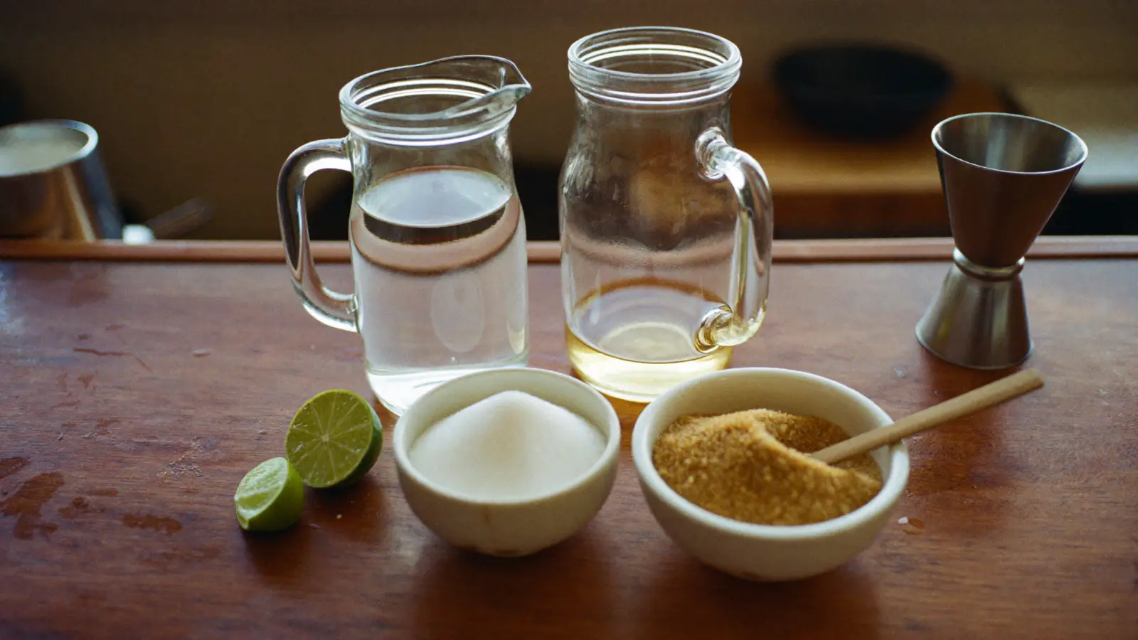 Sirop de sucre blanc et sirop de canne maison en carafes, avec des bols de sucre blanc et de sucre roux, un citron vert et un doseur