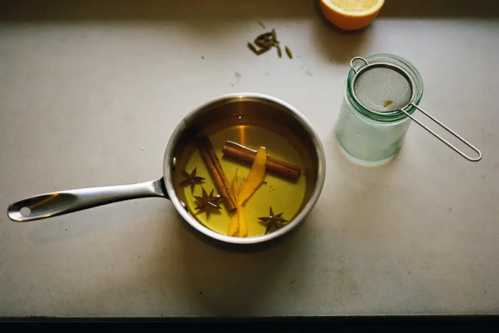 Casserole de sirop de sucre infusé à la cannelle, à la badiane et au zeste d'orange, avec un bocal et une passoire