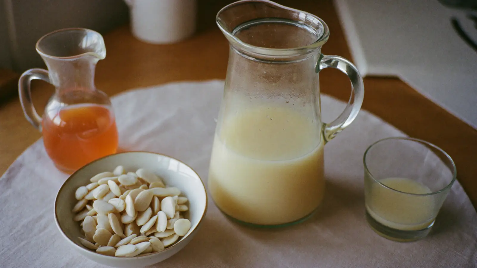 Carafe de sirop d'orgeat maison à côté d'un bol d'amandes mondées et d'un petit verre