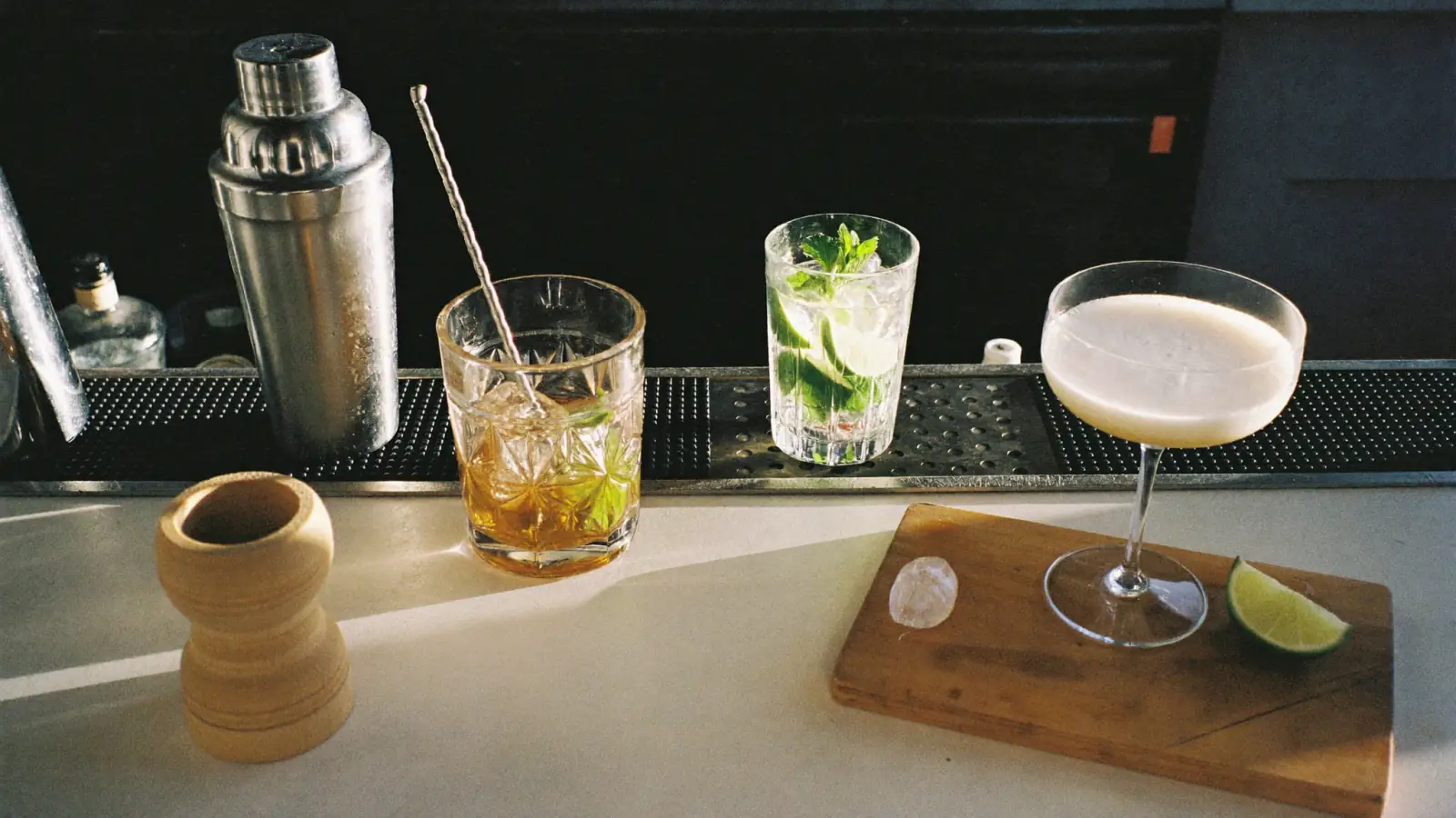 Shaker, cocktail remué avec sa cuillère de bar, long drink à la menthe et cocktail sour en coupe sur un comptoir de bar