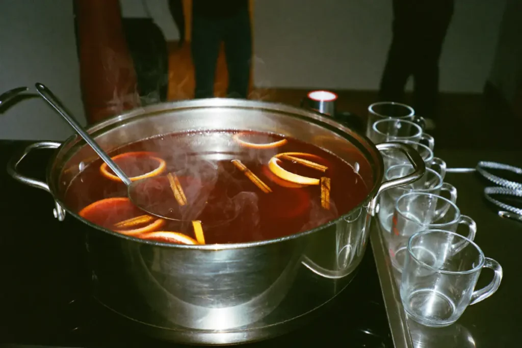Grande marmite de vin chaud à l'orange et à la cannelle sur feu doux, avec une louche et des mugs alignés pour une fête